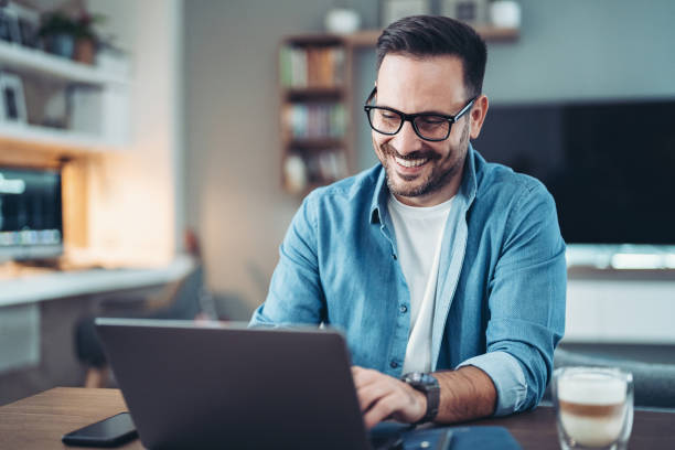 istock Smiling man using laptop in a living room 1952026399