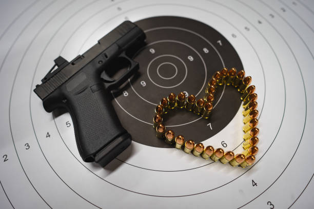 istock Theme of Valentine's day and weapons. A modern compact pistol with a red dot, a target and a heart made of 9mm cartridges. 1952067905