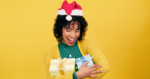 Happy woman, Christmas and gift box for festive season or December giving on a yellow studio background. Young female person with present and hat for giveaway, fashion or celebration on mockup space