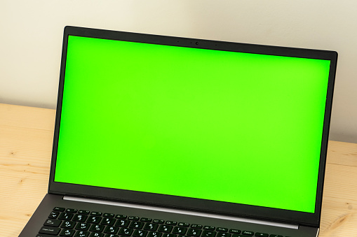 A photo of a laptop on a wooden desk showing a green screen.