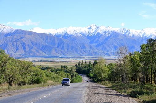 August 29 2023 - Karakol in Kyrgyzstan: street with cars to the snowy peaks behind the town