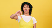 Frown, thumbs down and woman portrait in studio with rejection, denial or review disappointment on yellow background. Hands, emoji or face of female model with gesture for wrong, mistake or vote fail