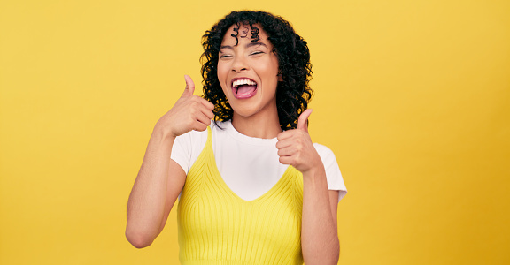 Excited, thumbs up and portrait of woman winning, success or achievement in studio isolated on a yellow background mockup space. Happy, fingers and like hand gesture, ok emoji and sign for agreement