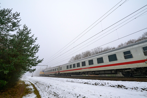 International train of the Dutch Railways driving through the snow on a cold day in the Veluwe nature reserve in winter.