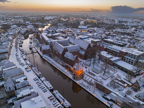 Zwolle snowy Thorbeckegracht during a cold winter morning seen from above with houseboats in the canal and the Broerenkerk church in the background. The rooftops a covered in a thin layer of snow.
