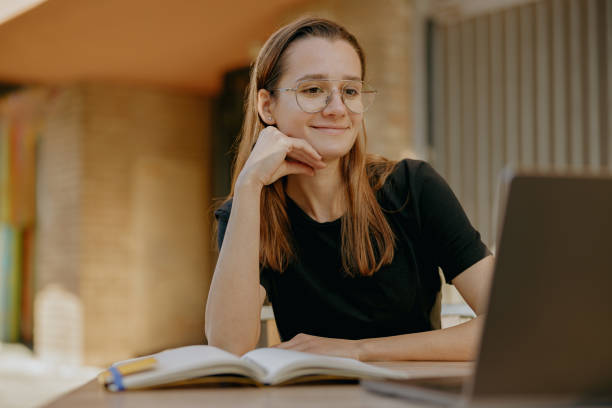 istock Smiling young female student studying on laptop while sitting on cafe terrace 1952159246