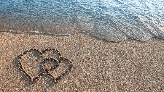 Two hearts painted on sand on the beach.