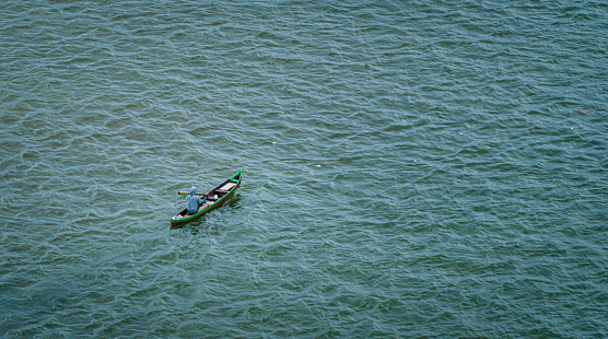 Ambon, Indonesia - January 21, 2024 : copy space photo of a fisherman rowing a boat in the middle of the blue sea