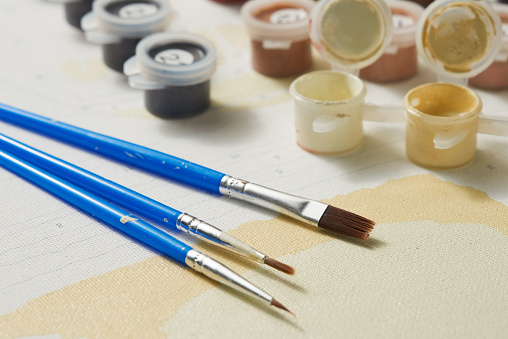 A set of brushes and jars of paint on canvas for painting by numbers.