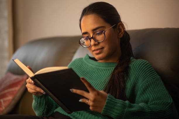 istock Serious woman reading novel on sofa at home 1952216496