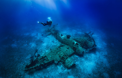 A scuba diver descending to a sunken world war two fighter propeller airplane at the seabed of the Aegean Sea, Naxos island, Greece