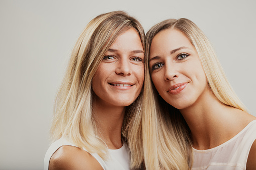 Blonde women, possibly siblings, share a cheerful moment, affectionately wrapped in an embrace