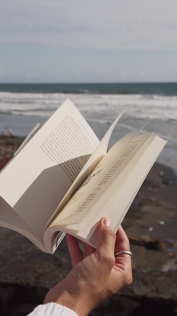 book in hands on the background of the ocean and waves. Vertical video
