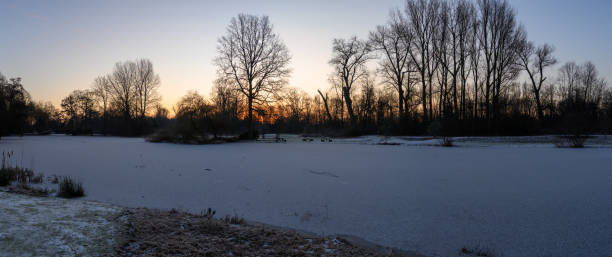 istock Scenic sunrise over a snow-covered pond and leafless trees. Deurne, Belgium 1952289426