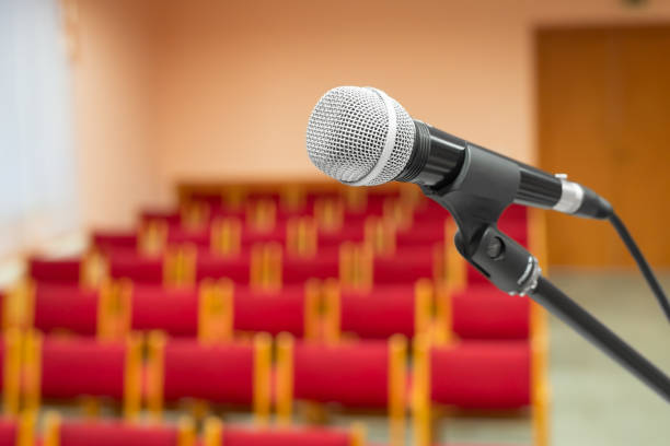 Audience sits waiting for the speaker at a conference. The microphone is in the foreground.