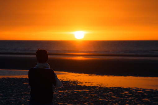 A woman's back looks at a sunset over the sea