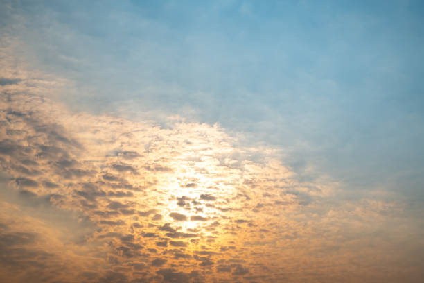 The sun breaks through fluffy, gilded clouds as it rises at the start of a new day. Lens flare from sunbeams.