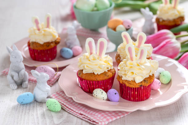 Carrot cake cupcakes for Easter. Carrot cupcakes with cream cheese frosting decorated with easter bunny ears on white wooden background. stock photo