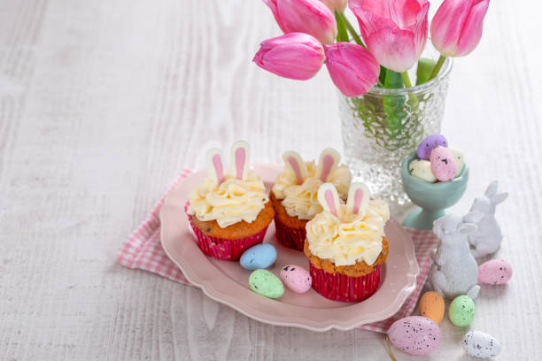 istock Carrot cake cupcakes for Easter. Carrot cupcakes with cream cheese frosting decorated with easter bunny ears on white wooden background. 1952351264