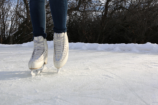 White ice skates worn by an unrecognizable figure skater standing stationary on an outdoor ice rink intentionally offset in the frame to create copy space.