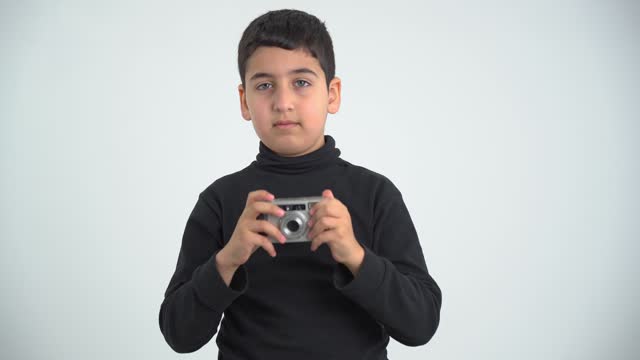 child holding an old film camera, aiming and shooting while looking forward, isolated on a gray background