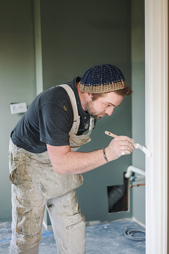 Young, skilled Painter & Decorator overcoming the disability of having one hand as he carefully and skilfully paints a door architrave in a residential house