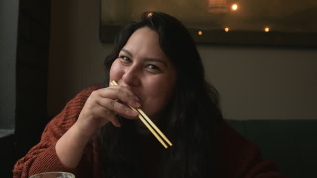 Woman, face and happy for eating with chopsticks in Japanese restaurant, shop or diner with laughing. Person, portrait and ramen or noodles for nutrition, healthy meal or fast food in a city cafe