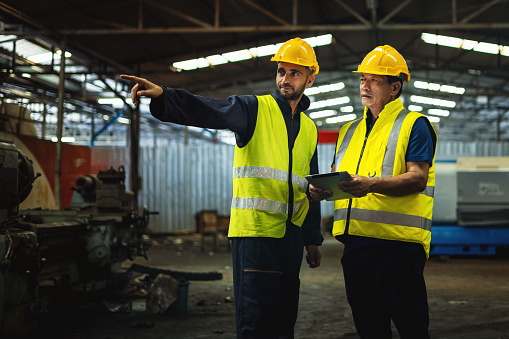 Warehouse and factory workers in uniform, wearing yellow hard hats and safety helmets, collaborate on an industrial site managed by foremen and engineers
