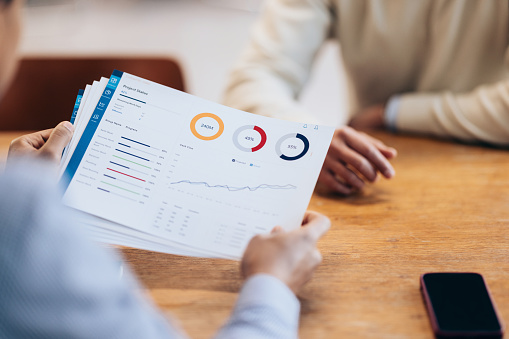 A close-up view of a financial report being held by one person during a meeting.