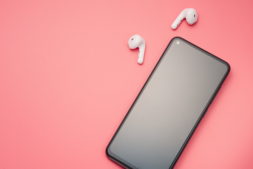 Smartphone and white wireless headphones on a pink background with copy space. Flat lay.