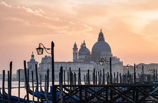 Looking out across a line of gondolas on the magnificent Grand Canal in Venice at sunset, with the majestically-domed Santa Maria della Salute Basilica in the background.