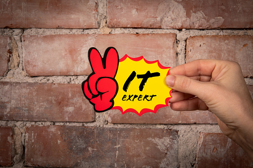 IT Expert. Sticky note with text on a red brick background.