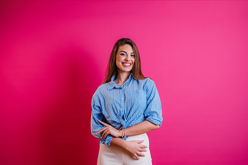 Portrait of a beautiful young woman standing in front of a bright pink background.