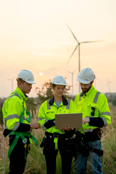 istock Vertical image group of technician workers man and woman work using laptop and stay in front of windmill or wind turbine with evening light. 1952441067