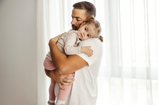 A tender father is holding his daughter in his arms and hugging her.