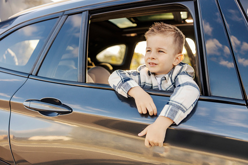 A cute little boy is sitting on the passenger's seat and leaning over window.