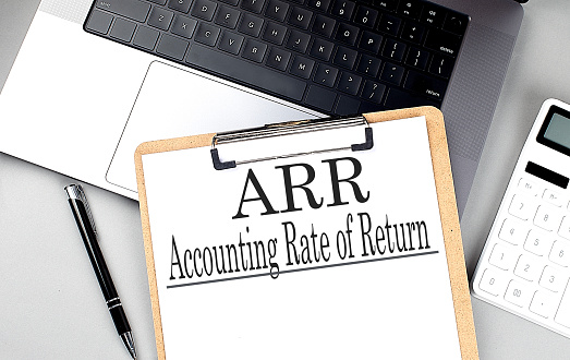 Paper clipboard with ARR ACCOUNTING RATE OF RETURN on a laptop with pen and calculator