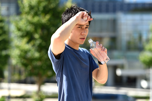 Young Asian man drinking water during break while running outdoors