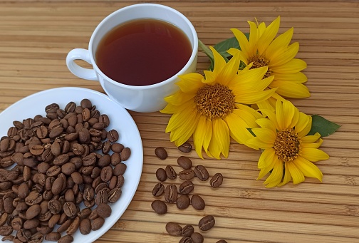 Coffee beans on a plate and a cup with coffee, sunflower flowers on the table.