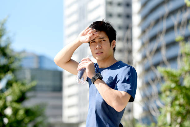 Young Asian man drinking water during break while running outdoors