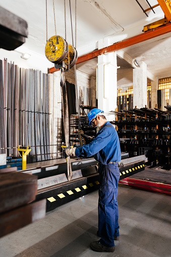 Side view of senior male construction worker in blue protective helmet and uniform working with hydraulic crane equipment in workshop