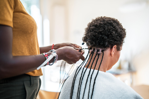 A mixed race female getting her hair braided by a mid-adult Black female in a cozy home setting.