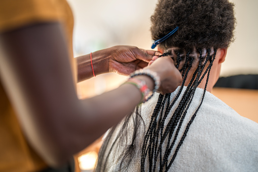 Close up of a mid adult Black female's hands skillfully creating braids on a mixed race female's hair in a domestic setting.