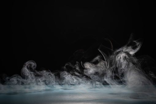 Dynamic movement of white smoke swirling elegantly against a contrasting dark backdrop in a studio environment.