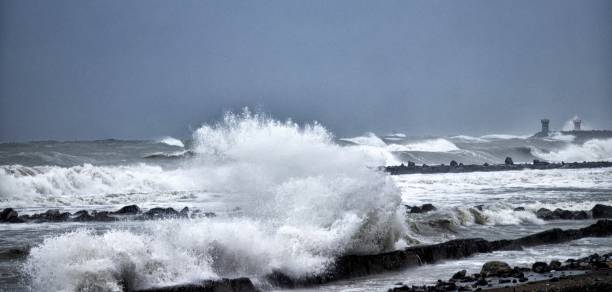 This photo shows a powerful wave crashing against the beach. The wave is immense, and it is sending up a spray of water.