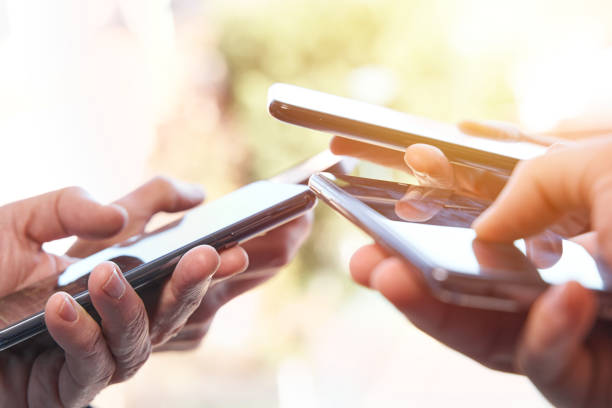 istock Four people's hands using smartphone on sunny summer afternoon. Connection and comunication 1952529066