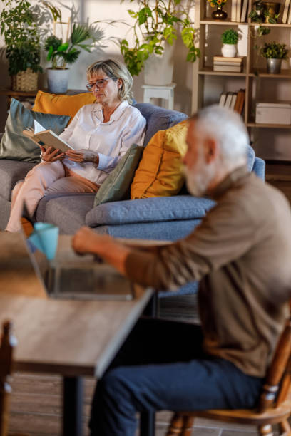 istock Mature man using laptop at dining table, his wife reading a book 1952553348