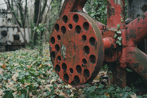 Detail of the rusted red wheel of an old unused air compressor in the forest. Industrial history machine. Iron and steel production. Abandoned machinery.