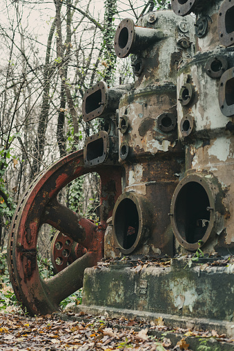 An old rusted air compressor with red colored wheel in the forest. Industrial history machine. Iron and steel production. Abandoned machine.