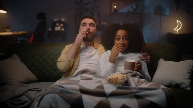 Two loving people sitting at sofa and watching series at free time, eating popcorn
